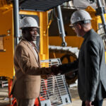 Multiracial engineers in work helmets shaking hands and making a deal during a meeting at an equipment manufacturing plant